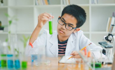 Asyalı erkek bilim öğrencileri mikroskopla bakıyorlar ve sınıfta bitki testleri yapıyorlar. Bitki türleri üzerinde bilimsel deneyler öğrenmek.