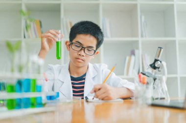 Asyalı erkek bilim öğrencileri mikroskopla bakıyorlar ve sınıfta bitki testleri yapıyorlar. Bitki türleri üzerinde bilimsel deneyler öğrenmek.