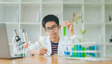 Asyalı erkek bilim öğrencileri mikroskopla bakıyorlar ve sınıfta bitki testleri yapıyorlar. Bitki türleri üzerinde bilimsel deneyler öğrenmek.