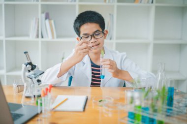 Asyalı erkek bilim öğrencileri mikroskopla bakıyorlar ve sınıfta bitki testleri yapıyorlar. Bitki türleri üzerinde bilimsel deneyler öğrenmek.