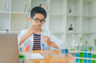 Asyalı erkek bilim öğrencileri mikroskopla bakıyorlar ve sınıfta bitki testleri yapıyorlar. Bitki türleri üzerinde bilimsel deneyler öğrenmek.