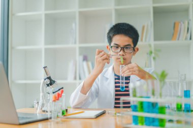 Asyalı erkek bilim öğrencileri mikroskopla bakıyorlar ve sınıfta bitki testleri yapıyorlar. Bitki türleri üzerinde bilimsel deneyler öğrenmek.