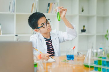 Asyalı erkek bilim öğrencileri mikroskopla bakıyorlar ve sınıfta bitki testleri yapıyorlar. Bitki türleri üzerinde bilimsel deneyler öğrenmek.