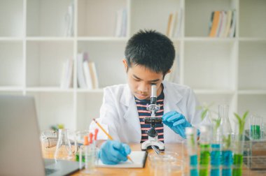 Asyalı erkek bilim öğrencileri mikroskopla bakıyorlar ve sınıfta bitki testleri yapıyorlar. Bitki türleri üzerinde bilimsel deneyler öğrenmek.