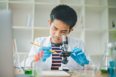 Asyalı erkek bilim öğrencileri mikroskopla bakıyorlar ve sınıfta bitki testleri yapıyorlar. Bitki türleri üzerinde bilimsel deneyler öğrenmek.