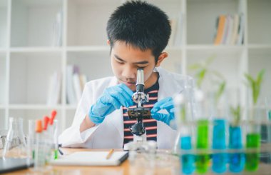 Asyalı erkek bilim öğrencileri mikroskopla bakıyorlar ve sınıfta bitki testleri yapıyorlar. Bitki türleri üzerinde bilimsel deneyler öğrenmek.