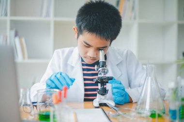 Asyalı erkek bilim öğrencileri mikroskopla bakıyorlar ve sınıfta bitki testleri yapıyorlar. Bitki türleri üzerinde bilimsel deneyler öğrenmek.