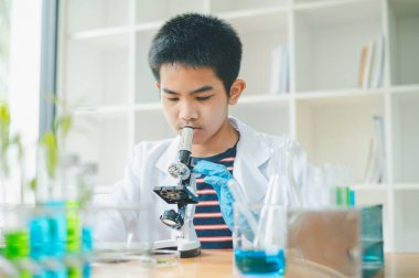 Asyalı erkek bilim öğrencileri mikroskopla bakıyorlar ve sınıfta bitki testleri yapıyorlar. Bitki türleri üzerinde bilimsel deneyler öğrenmek.