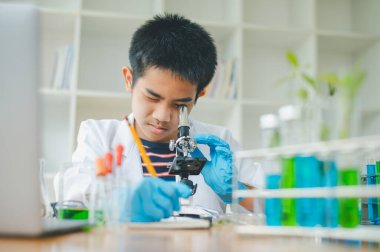 Asyalı erkek bilim öğrencileri mikroskopla bakıyorlar ve sınıfta bitki testleri yapıyorlar. Bitki türleri üzerinde bilimsel deneyler öğrenmek.