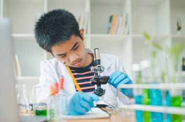 Asyalı erkek bilim öğrencileri mikroskopla bakıyorlar ve sınıfta bitki testleri yapıyorlar. Bitki türleri üzerinde bilimsel deneyler öğrenmek.