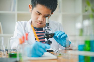 Asyalı erkek bilim öğrencileri mikroskopla bakıyorlar ve sınıfta bitki testleri yapıyorlar. Bitki türleri üzerinde bilimsel deneyler öğrenmek.