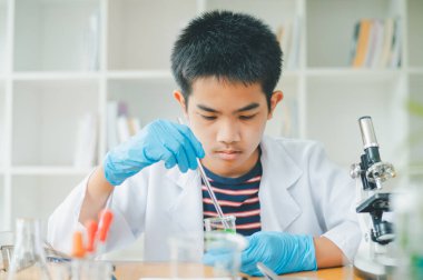 Asyalı erkek bilim öğrencileri mikroskopla bakıyorlar ve sınıfta bitki testleri yapıyorlar. Bitki türleri üzerinde bilimsel deneyler öğrenmek.