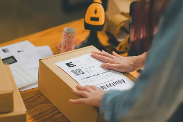 startup young female small business owners attaching shipping labels to cardboard boxes or parcels for delivery of customer orders-concept shopping online