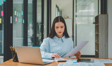 Asyalı iş kadını ahşap masa, vergi, muhasebe, istatistik ve analitik araştırma kavramında matematik finansmanı için dizüstü bilgisayar kullanıyor.