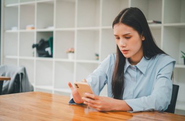 İnternet 'te e-posta ya da sosyal medyayı kontrol ederken cep telefonu kullanan Asyalı iş kadını masasında oturuyor.