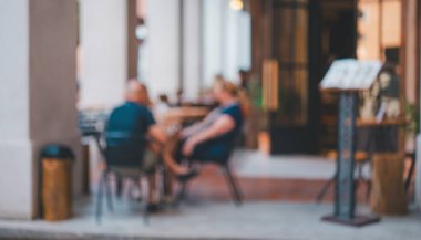 Bir adam ve bir kadının masada oturduğu bir restoranın bulanık görüntüsü. Adam mavi bir gömlek giyiyor ve kadın mavi bir gömlek giyiyor. Sandalyeler boş.