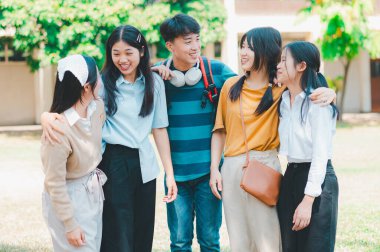 Bir grup genç bir parkta birlikte duruyorlar. Gülümsüyorlar ve birbirlerine sarılıyorlar.