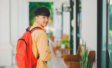 Öğrenmek için okula giderken elinde kitapla mutlu gülümseyen bir öğrenci..