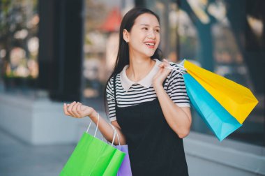 Bir kadın bir sürü alışveriş çantası tutuyor ve gülümsüyor. O siyah bir elbise ve beyaz bir gömlek giyiyor.