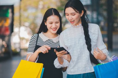 İki kadın alışveriş torbaları tutarken cep telefonuna bakıyor. Telefondaki bir şeyi kontrol ediyorlar gibi görünüyor, muhtemelen bir alışveriş listesi ya da kupon.