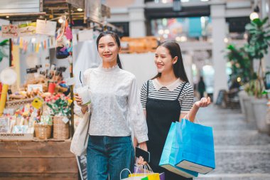 İki kadın sokakta yürüyordu, biri mavi bir çanta tutuyordu. Diğer kadın beyaz bir çanta tutuyor. İkisi de gülümsüyor ve alışveriş gezilerinden zevk alıyor gibi görünüyorlar.