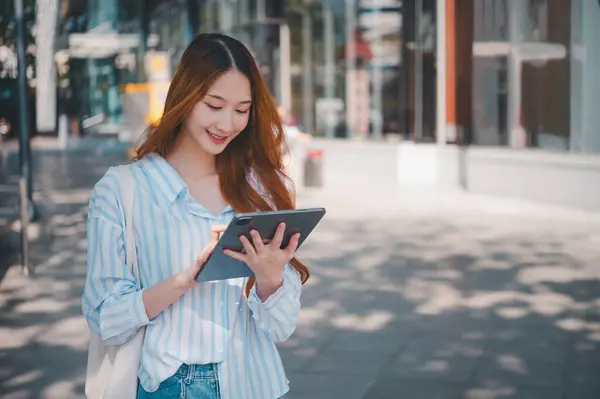 A woman is walking down the street with a tablet in her hand. She is smiling and she is enjoying her time