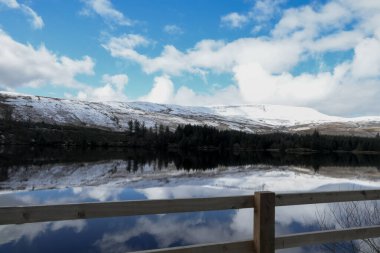 Kış manzarası ve yansımaları Brecon Beacons Ulusal Parkı 'ndaki Galler rezervuarının suyunda kar ve buzla kaplı buzlu dağ tarafını ve yukarıda bulutlu gökyüzünü gösteriyor.. 