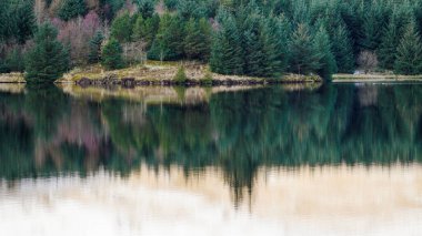 Kış manzarası ve yansımaları Brecon Beacons Ulusal Parkı 'ndaki Galler rezervuarının suyunda kar ve buzla kaplı buzlu dağ tarafını ve yukarıda bulutlu gökyüzünü gösteriyor.. 