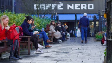 Cardiff, Wales, 29 Ekim 2023: Sokak fotoğrafçılığı, Cardiff şehir merkezinde yoğun bir öğleden sonra. Hayes 'teki Cafe Nero' nun dışındaki banklarda oturan insanlar. Onlar öğle yemeklerini yiyor ve kahve içiyorlar..
