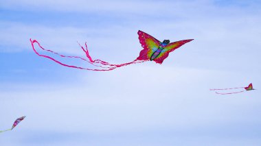 Kelebek şekilli uçurtma, Knap 'te bir aile uçurtma festivalinde uçuruluyor Barry. Uzun kuyruğu rüzgarı yakalar ve yükselir. Şekil, ince bulutlarla dağılmış mavi gökyüzüne karşı duruyor..