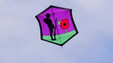 Movie of a purple and green kite fying in the air, the decoration is to honour the fallen, with a red poppy and a silhouette of a soldier with a gun. Background for poppy day, remembrance sunday,