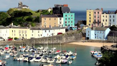 Tenby, Pembrokeshire, Galler: 3 Temmuz 2024: 4K videosu, Tenby 'nin kuzey sahilindeki limanda demirlemiş tekneler. Resmedilmeye değer pastel evler limana kadar uzanan sarp bir tepe ile kasabaya yükseliyor..