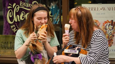 Tenby, Pembrokeshire, Galler - 02 Temmuz 2024: Anne ve kız tatlı bir ziyafetin tadını çıkarın. Kız waffle dondurması yiyor ve anne külah yiyor. Seçimlerinden çok memnunlar.