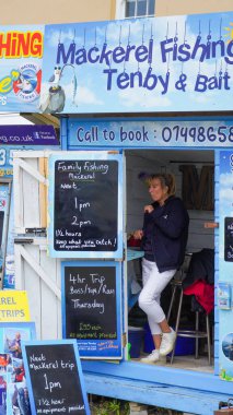 Tenby, Pembrokeshire, Galler - 02 Temmuz 2024: Limanın girişinde balıkçılık ve gezi gezileri satan küçük kulübeler bulunmaktadır. Parlak mavi işaretler canlı, göz alıcı ve bilgilendiricidir..