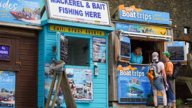 Tenby, Pembrokeshire, Galler - 02 Temmuz 2024: Limanın girişinde balıkçılık ve gezi gezileri satan küçük kulübeler bulunmaktadır. Parlak mavi işaretler canlı, göz alıcı ve bilgilendiricidir..