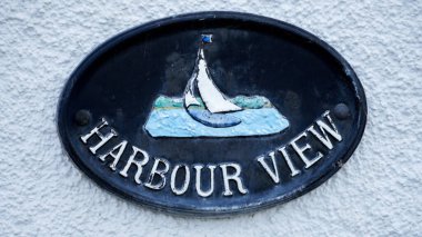 A stone wall with a decorative oval plaque saying Harbour View. One of the many coastal and beach inspired house names in Tenby reflecting locations close to the harbour of this popular Welsh resort  clipart