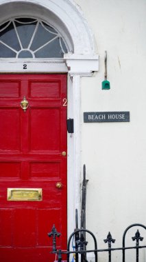 A red front door a name plaque saying beach house. One of the many coastal and beach inspired house names in Tenby reflecting locations close to the beaches and harbour of this popular Welsh resort  clipart