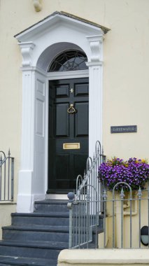Üzerinde Sheerwater yazan, dikdörtgen bir levha olan, soluk, krem rengi taştan bir duvarlı, siyah bir ön kapı. Galler 'in Tenby tatil beldesindeki plajlardan biri.. 