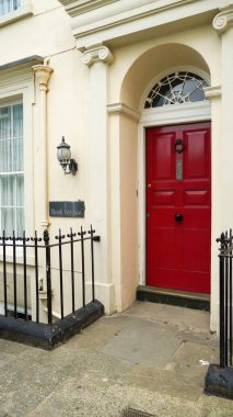 A cream stone wall with a rectangular plaque with the name Rock Terrace etched on it and a red front door. One of many coastal and beach inspired house names in the seaside resort of Tenby, Wales.  clipart