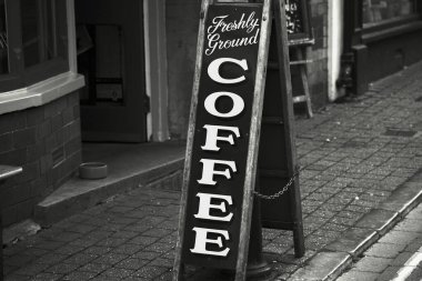 Tenby, Pembrokeshire, Galler Temmuz 02 2024: Tenby 'nin ana caddesinde uzun, ince ve serbest bir tebeşir tahtasında taze öğütülmüş kahve reklamı yapan bir tabelanın siyah beyaz fotoğrafı.