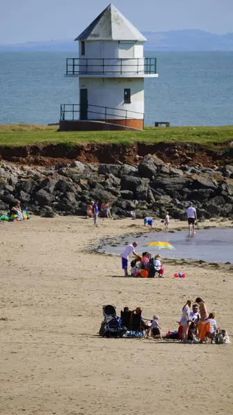 stock image Porthcawl, Bridgend, Wales - August 16 2024: Crowds of people on Coney Beach in Porthcawl enjoying the hot August sun. Children play on the sand and bathe in the sea with the old lighthouse behind.