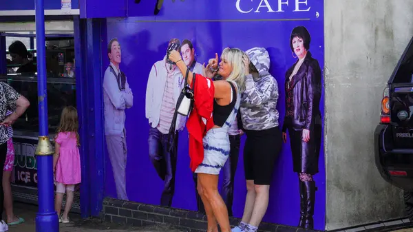 stock image Barry Island, Vale of Glam, Wales, Aug 30 2024: A female taking a selfie against a wall with portraits of the cast members of the Gavin and Stacey series outside Marco's cafe.