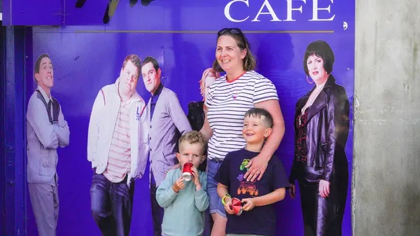 stock image Barry Island, Vale of Glam, Wales, Aug 30 2024: Visitors to Barry Island and fans of Gavin and Stacey take selfies against a wall with portraits of the cast members of the series outside Marco's cafe.