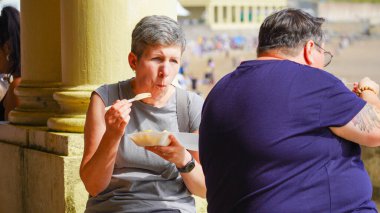 Barry Adası, Glamorgan Vadisi, Galler: 27 Ağustos 2024: Barry Adası 'ndaki duvarda duran tepside duran cips yiyen bir adam ve kadın. Geleneksel bir deniz kenarı yemeği ve güneşli bir günde bir ziyafet..