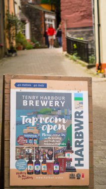 Tenby, Pembrokeshire, Wales - July 01 2024: Easel board with poster advertising Tenby Harbour Brewery at the entrance of Sergeants Lane which runs from the town centre to the harbour. clipart