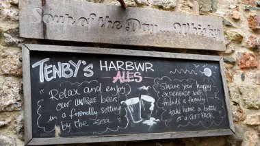 Tenby, Pembrokeshire, Galler - 01 Temmuz 2024: Kasaba merkezinden limana kadar uzanan Tenby Harbour Bira Fabrikası bar, dükkan ve menü çavuşları Yolu ilanlarıyla tebeşir tahtası.