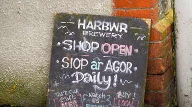 Tenby, Pembrokeshire, Wales - July 01 2024: Chalk board with signs advertising Tenby Harbour Brewery bar, shop and menus Sergeants Lane which runs from the town centre to the harbour. clipart