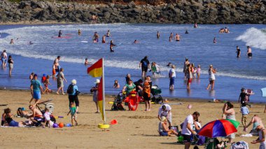 Porthcawl, Bridgend, Wales - Aug 15b 2024: Coney Beach in Porthcawl on a busy summer's day with the weather warm enough for swimming RNLI lifeguards are present at the water's edge to keep people safe clipart