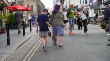 Tenby, Pembrokeshire, Galler, Temmuz 09: 2024: Dövmeli bacaklı bir kadın ve oğlu Tenby limanından kasabaya geri dönüyor. Denizden gelen taze balıklarla dolu bir halat taşıyor.