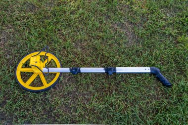 Teleskop sapı boyuna bantlanmış, çimlerin üzerinde duran bir tekerlek cihazı.